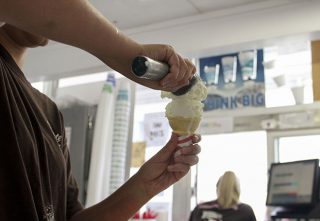 Employee Shelby Susnick scoops some vanilla ice cream into a cone for one of her customers, while fellow employee Kari Bland takes orders. "They started [making vegan ice cream] when I first started working here,"said Susnick."A lot of costomers can't eat dairy."