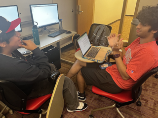 Two students converse while working on their laptops