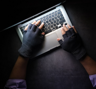 A person wearing fingerless gloves types on a computer