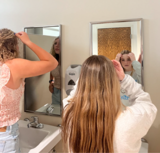 Two people look at their reflections and fix their hair while looking in the mirror