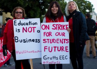 People hold up posters regarding education and students in pink and black font