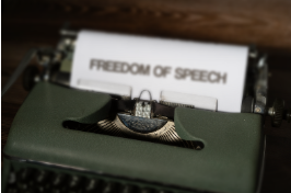 A typewriter presents a page that reads "FREEDOM OF SPEECH"