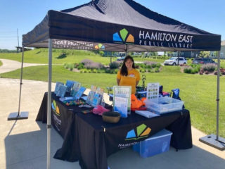 A person stands at a booth for the Hamilton East Public Library