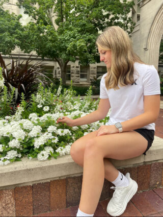 A woman sits beside a raised flowerbed and touches the flowers.