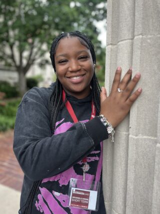 A woman leans against a stone wall to pose for a photo.