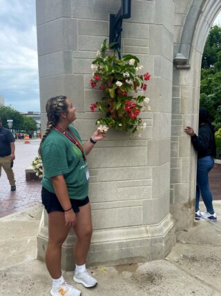 A woman touches flowers that are hanging on a stone pillar.