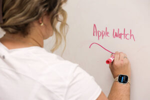 Alt: Woman writes on a white board while getting a text on Apple Watch.