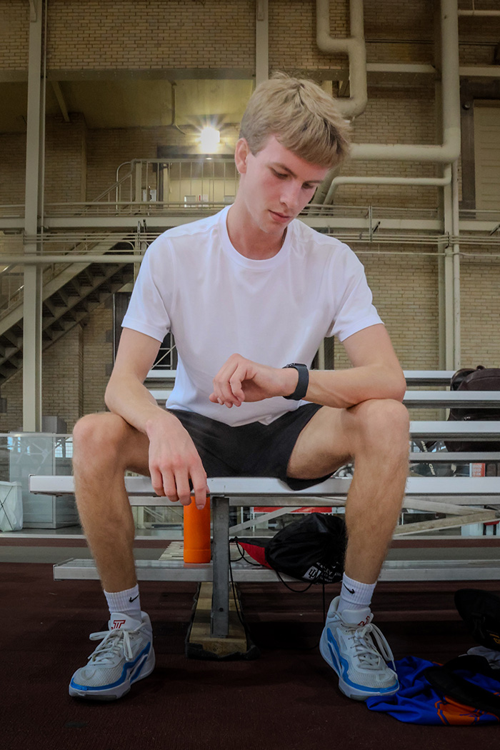 Man sits on bleachers at basketball court, looking at his Apple Watch.