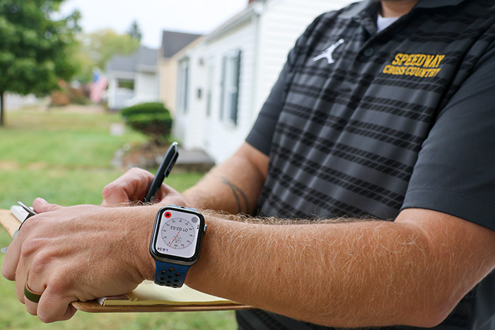 Man holding writing pad on clipboard and pen, writing the times displayed on his Apple Watch stopwatch.