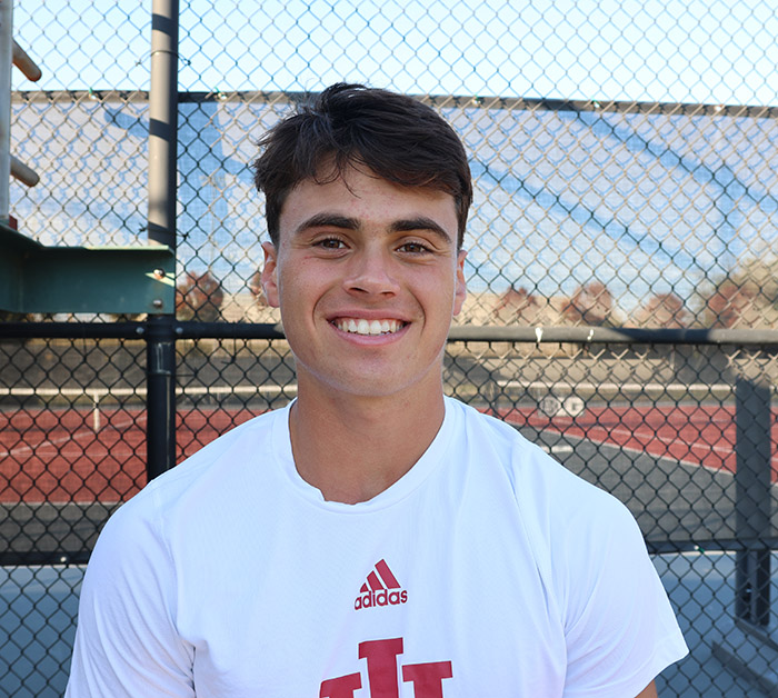 A young man smiles for the camera at the tennis courts after practice and an interview. 