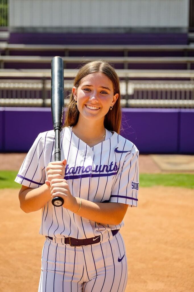 close up image of young woman posing on a softball field holding a bat