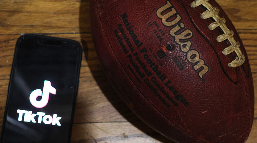 A phone, open to the popular app Tik Tok, lays next to a football.