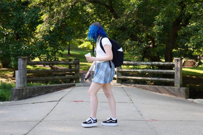 A vibrant student walks to class with her coffee in hand and music playing in her ears. Credit: Meredyth Jones