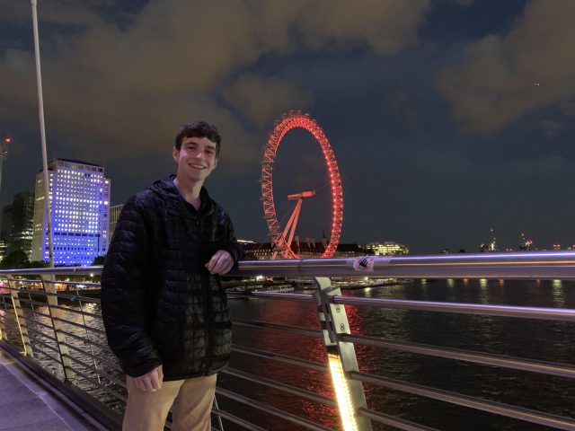 Drew Frey poses next to the famous London Eye ferris wheel at night.