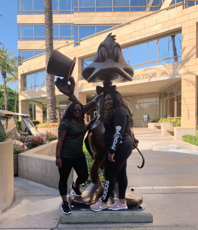 Two women posing with a Daffy Duck statue