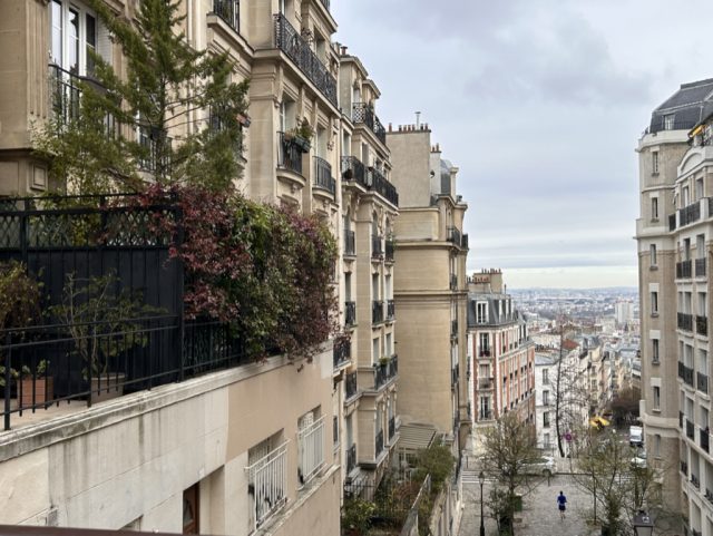 buildings line a cobblestone street in Paris with clouds in the sky in the background